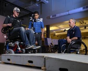 Man standing with two other men in wheelchairs 