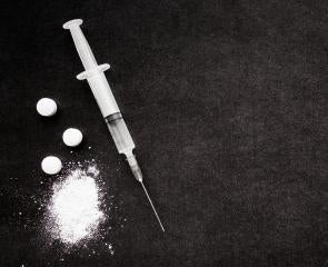 Syringe next to crushed pills in front of black background