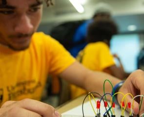 a student in a yellow Pitt shirt working with wires