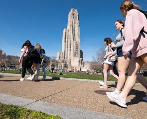 Groups of students walk by Schenley Plaza, with the Cathedral of Learning in the background