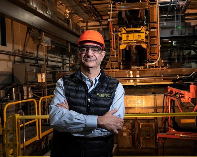 Carniero, wearing an orange hardhat, stands in an industrial factory