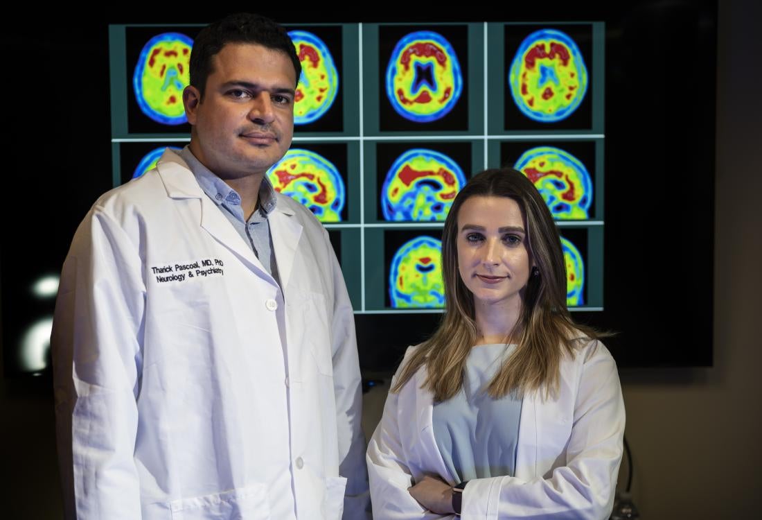 A man and a woman stand in front of photos of brain scans.