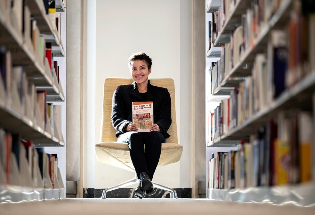 Roberts sits holding her book at the end of two library stacks