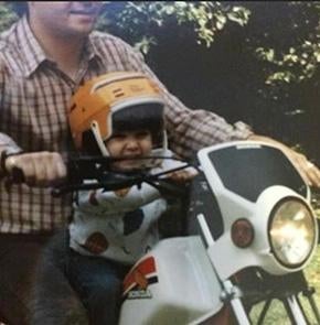 A toddler on someone's lap on a motorbike.