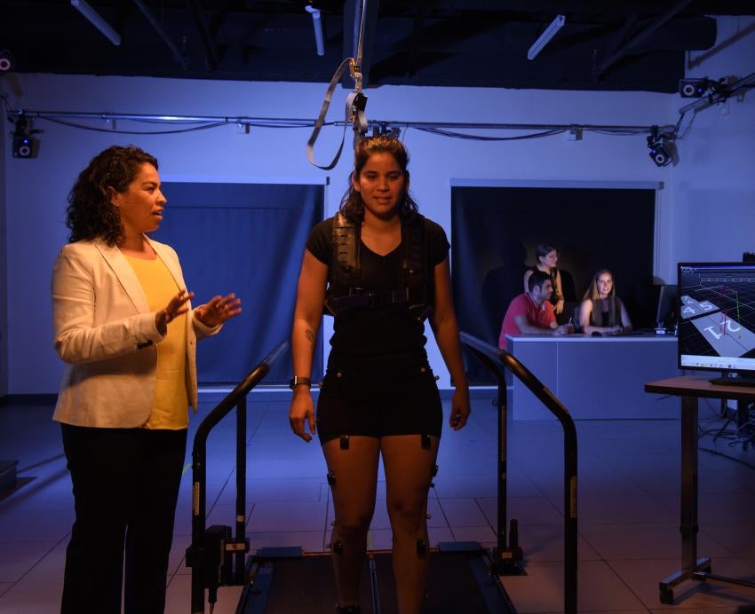 a person on a treadmill attached to ropes above with a person standing next to her