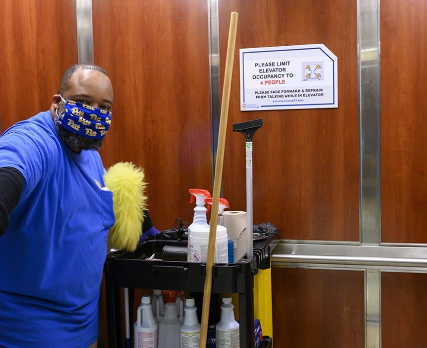 Cleaner in an elevator with cleaning supplies, blue uniform and mask