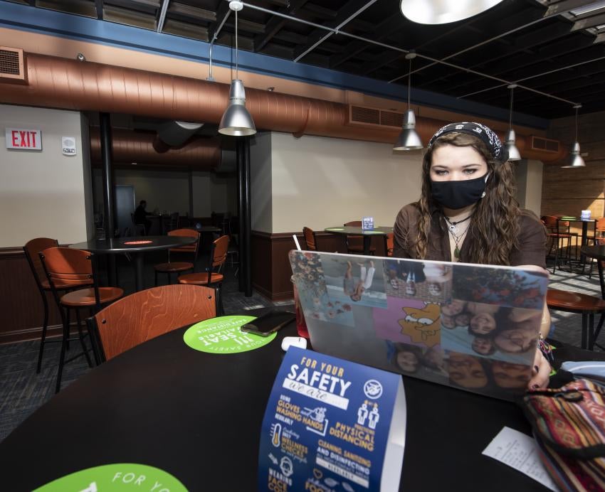 Woman in a mask sits at a table in a dining hall