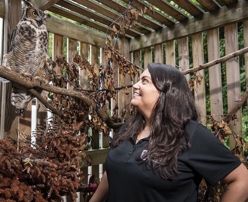 Katie Kefalos stands in an enclosure with an owl on a branch at her side