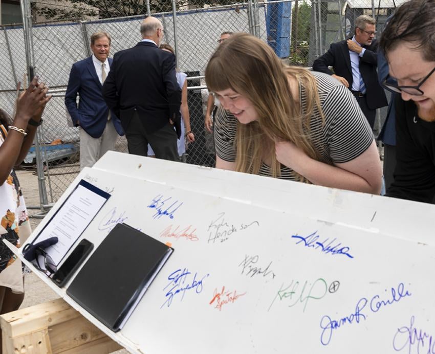 A man and woman sign a beam while another woman takes a picture on a phone
