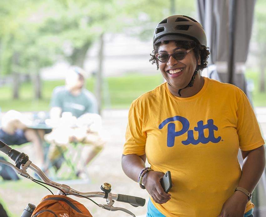 Woman in yellow Pitt shirt wearing helmet with bicycle 