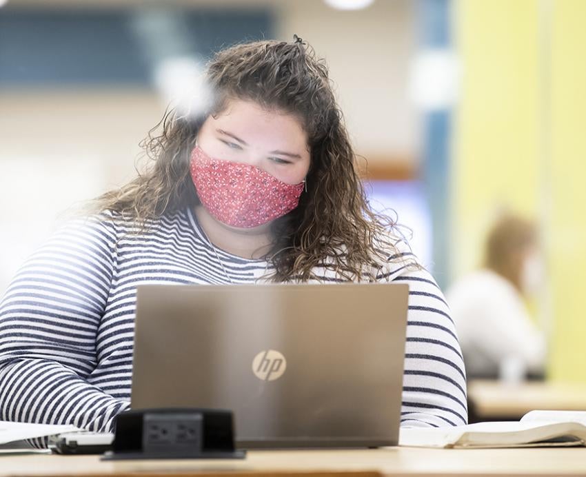 Student with red mask working on laptop 