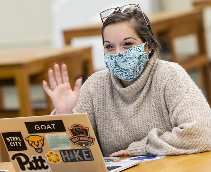 Student with mask using laptop, waving during video call