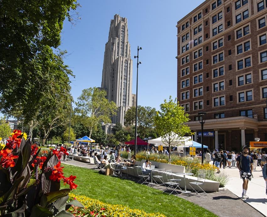 Cathedral of Learning towering behind flowerbed and busy sidewalk