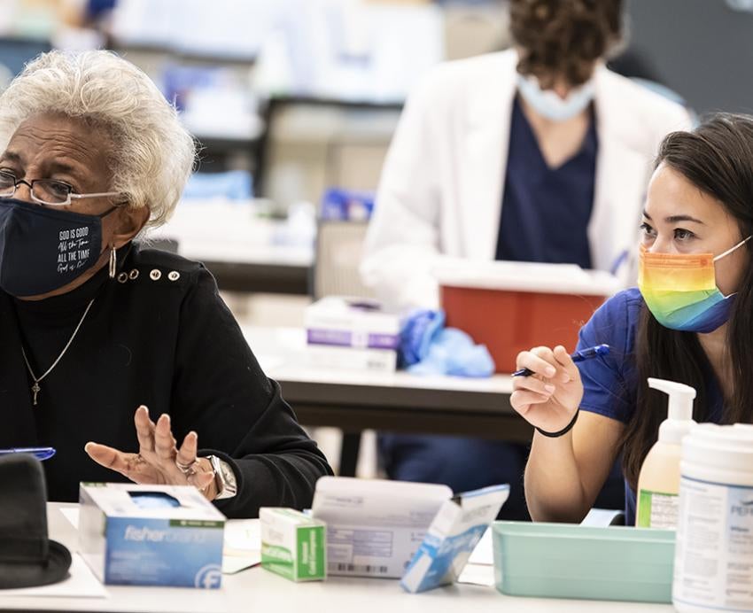 Two women with masks sitting at table at vaccine clinic