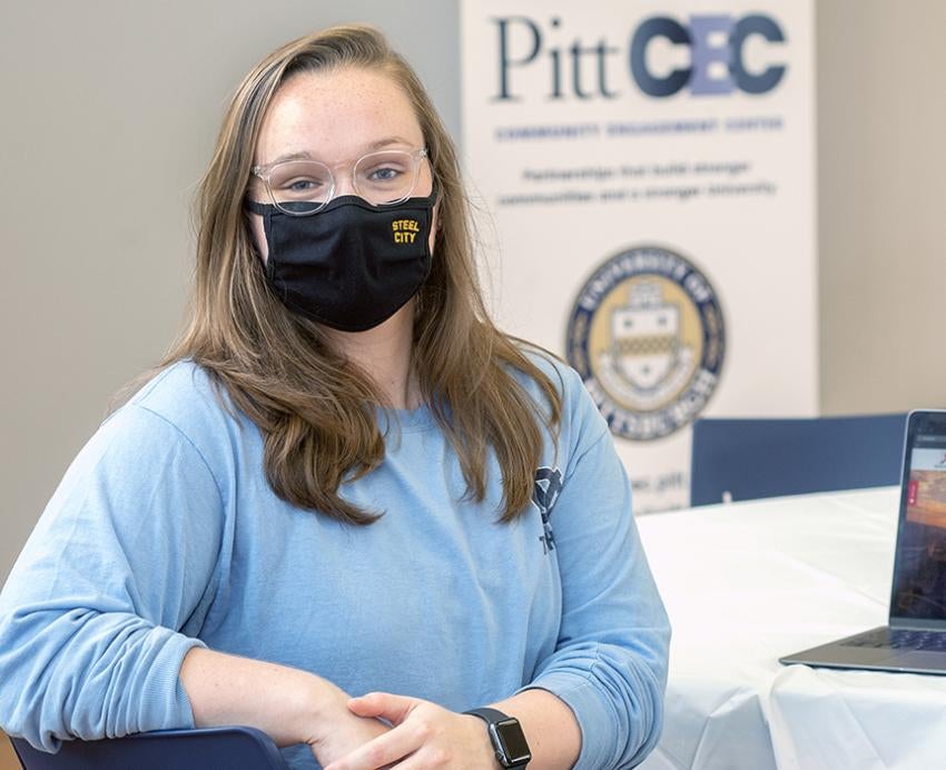 Julia Donnelly sitting in front of laptop with Pitt CEC banner in background