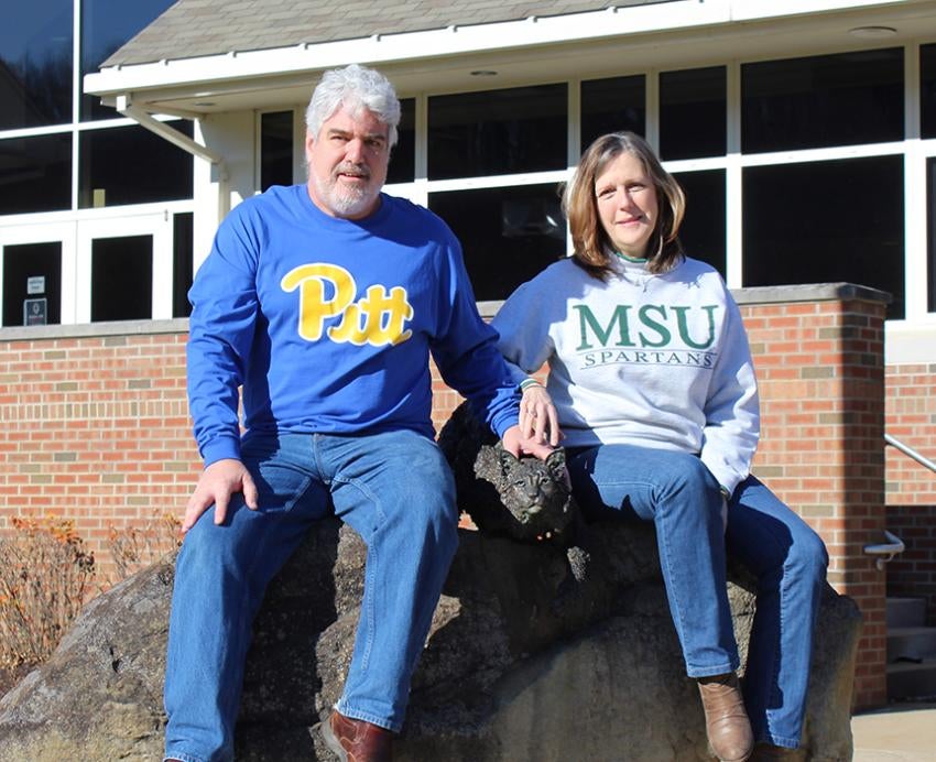 Gayle and Bill Pamerleau sitting on a rock, Galye with MSU sweater and Bill with Pitt sweater