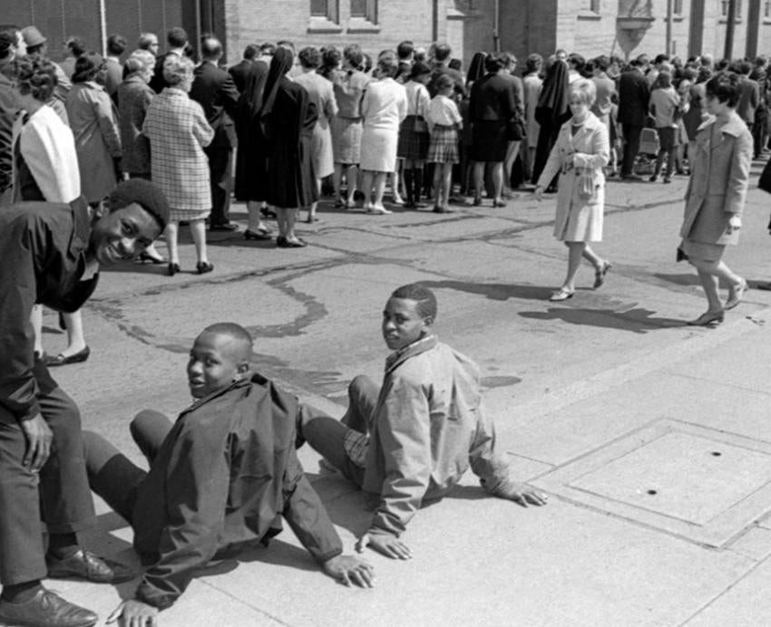 crowd of people gathered on street/sidewalk near a church with three boys in the foreground on National Day of Mourning following Martin Luther King Jr.'s assassination in 1968.