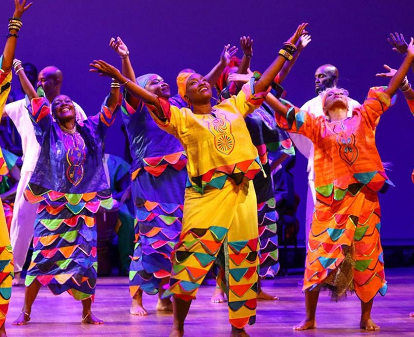 The KanKouran West African Dance Company dancing on stage in bright yellow and orange attire. 