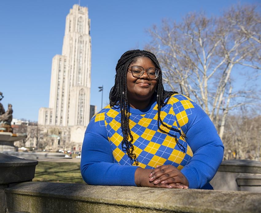 Haliyat Oshodi wearing blue and gold sweater posing in front of the Cathedral of Learning