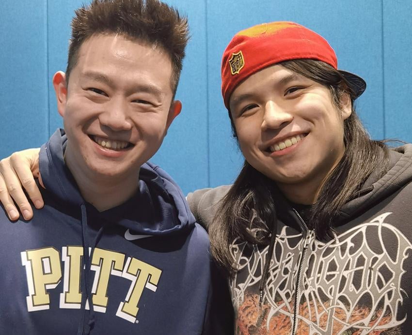 Adam Change wearing Pitt hoodie and posing for photo with a friend in orange hat