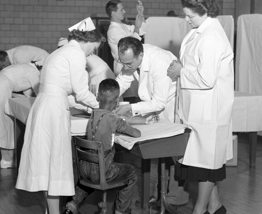 Old photo of Jonas Salk with nurses helping a child