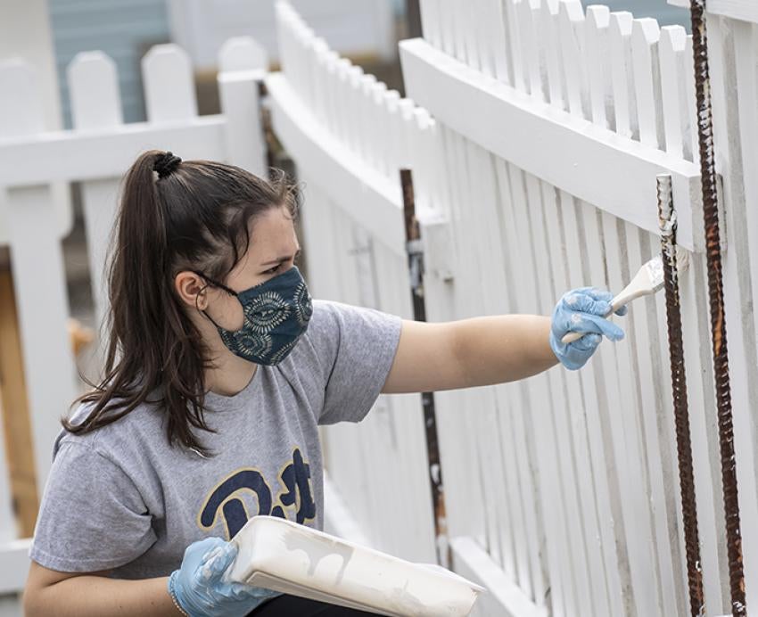 Student volunteer painting white fence
