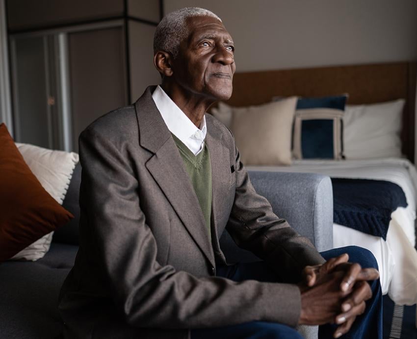 Elderly man in suit sitting on bed looking out of window