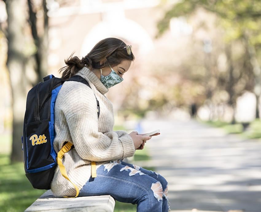 Pitt student using cellphone on bench outside