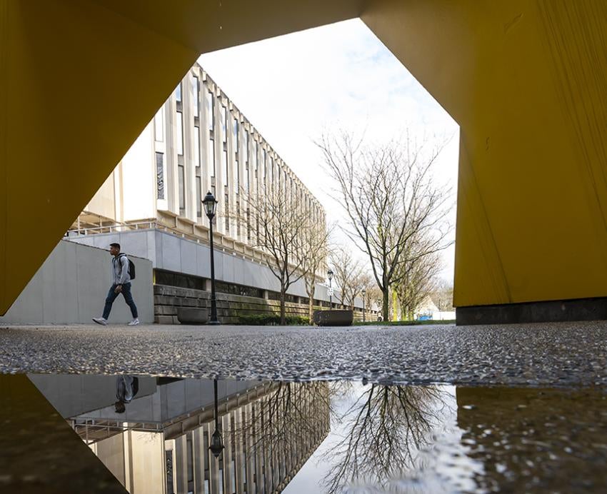 Student walking near large yellow sculpture on campus