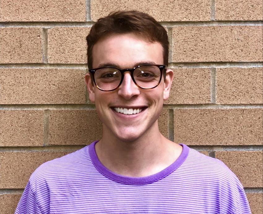 Tate Yawitz wearing purple shirt and glasses in front of brick wall