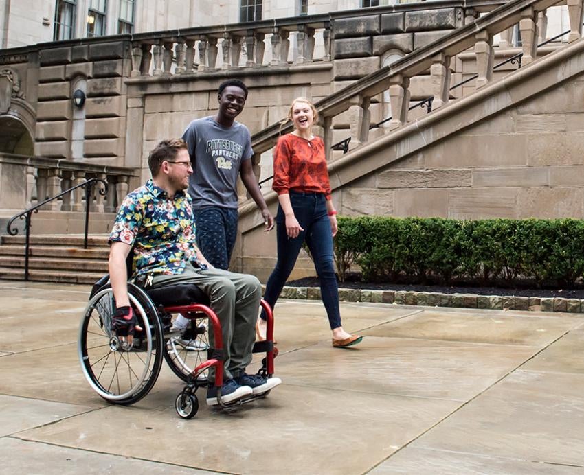 three people, one using a wheelchair, in front of the Cathedral