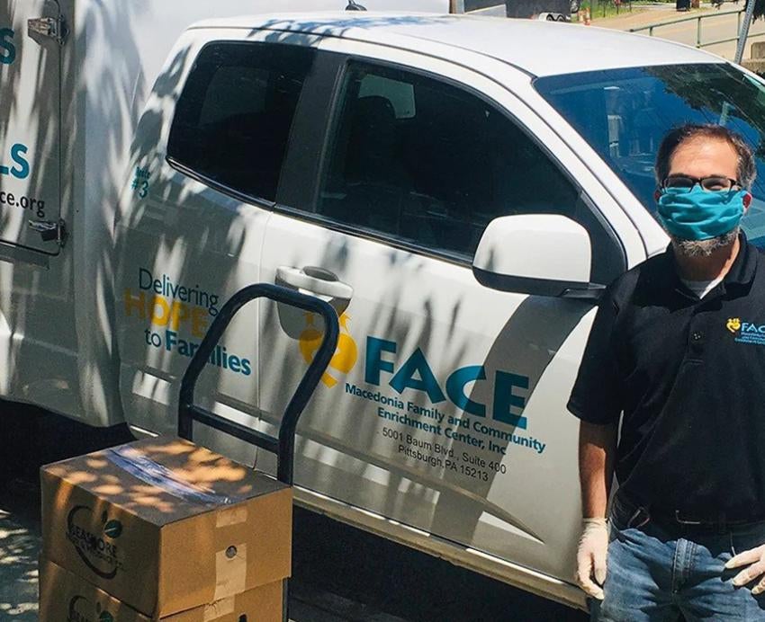 Justin LeWinter in a blue face mask standing next to a truck and a pile of cardboard boxes