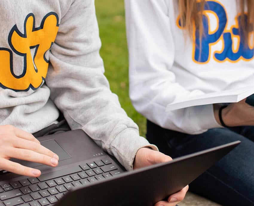 Pitt students sitting outside with laptop and book