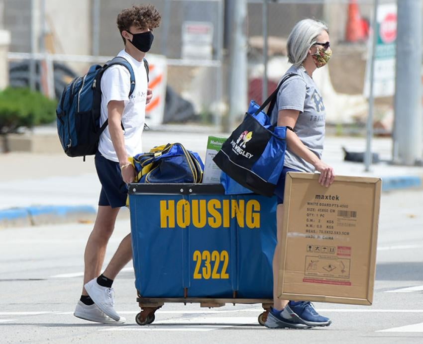 a student and adult pushing a full blue and gold housing cart across the street