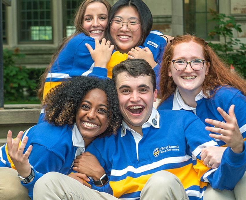 5 students in blue and gold shirts hugging and smiling