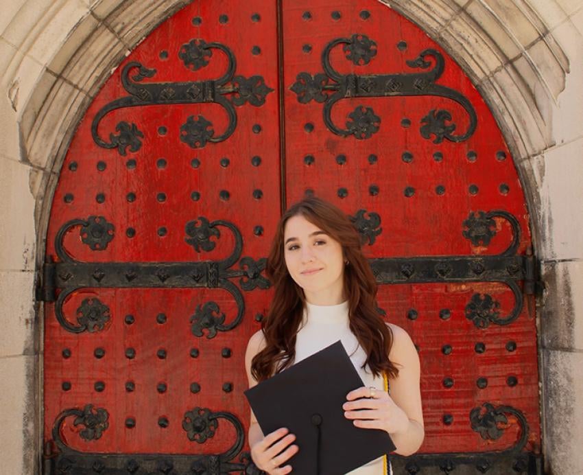a student holding a mortar board in front of a red door