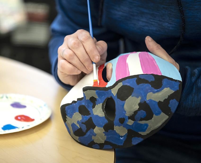 a person painting a mask split in half with stripes on one side and camo on the other