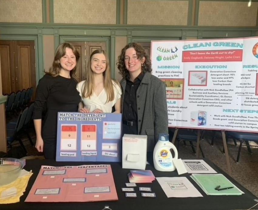 Three students stand behind a table with informational materials about laundry detergent. A poster board behind them says Clean Green.