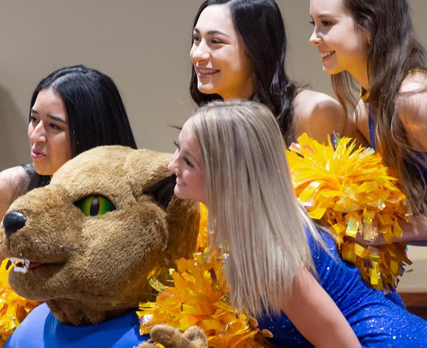 Cheerleaders with yellow pom poms pose with Roc the Panther
