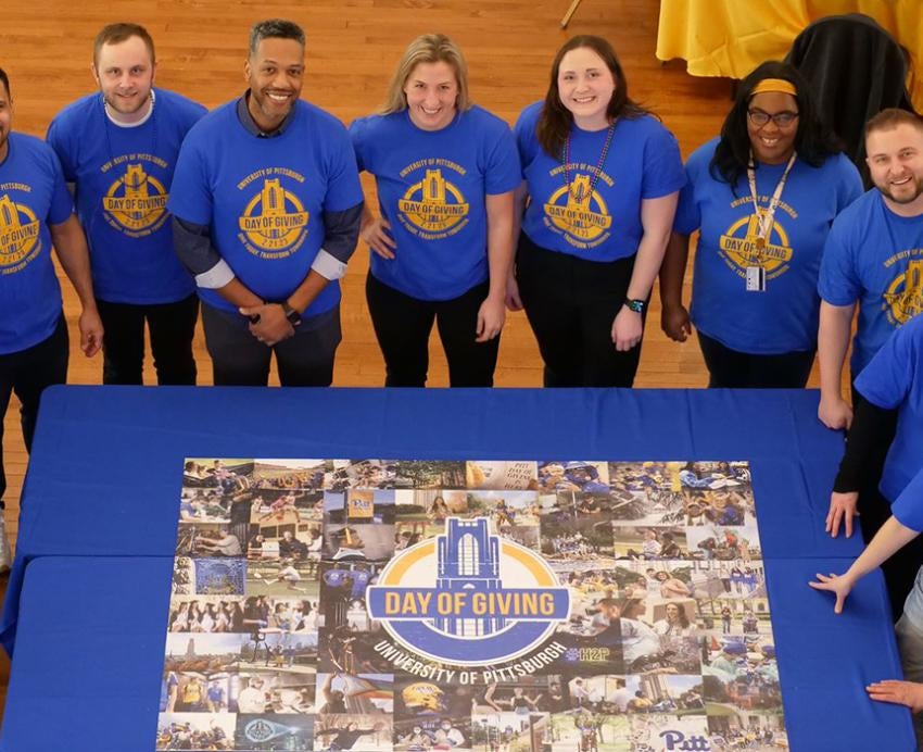 People in blue shirts gather around a Pitt Day of Giving puzzle