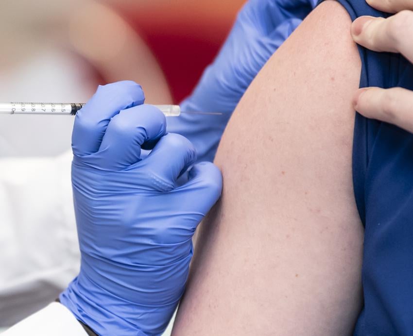 a gloved hand injecting a vaccine into an arm