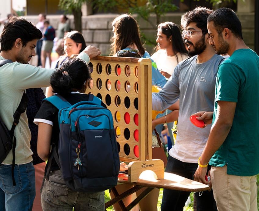 Students drop black and red discs into a large wooden Connect Four board