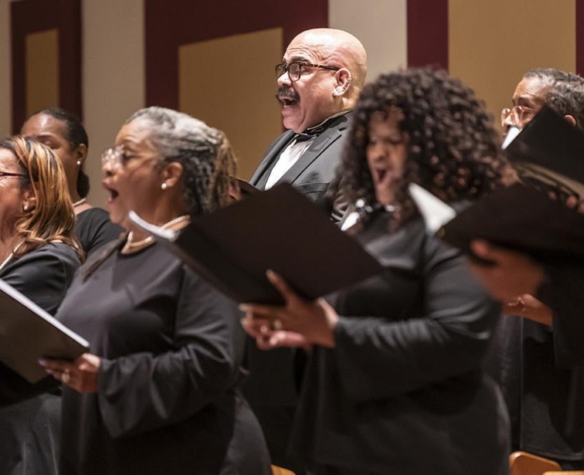 A choir wearing black sings from black folders
