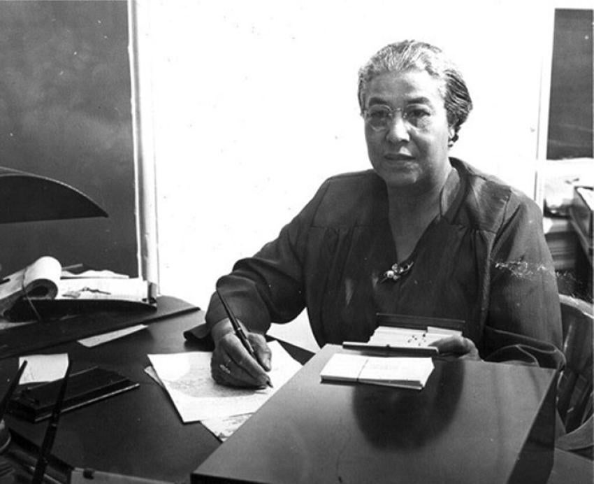 A black-and-white photo of Ella P. Stewart writing on paper at a desk