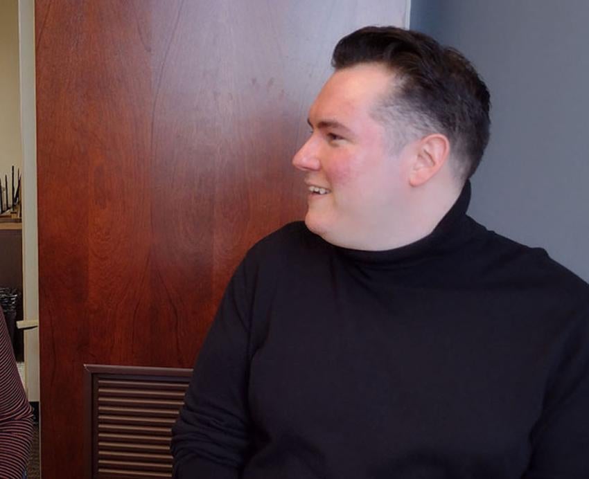 A person in a brown shirt smiles at a person in a black turtleneck