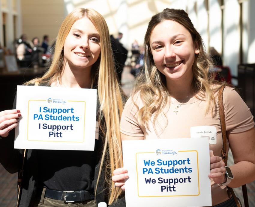 two people holding "We support PA students, we support Pitt" signs