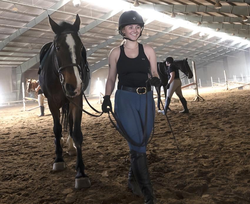 Girls lead horses across the inside of a barn