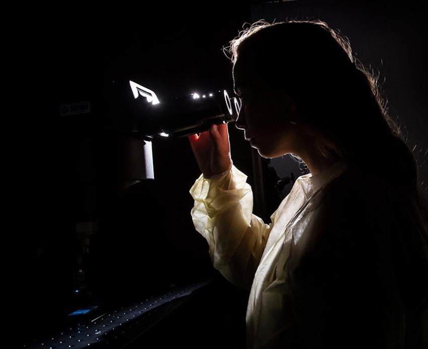 A person looks through a microscope in a dark room