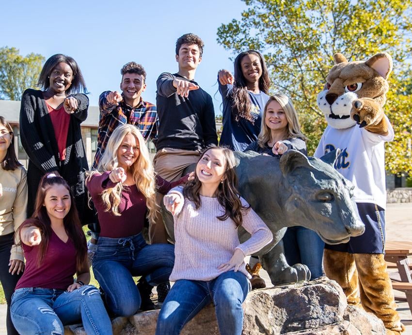 A group of students and a mascot sitting around a panther statue point at the camera