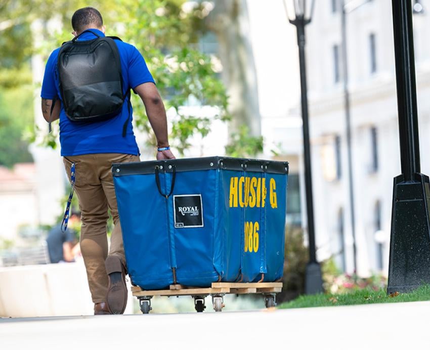 A person with a backpack rolls a blue housing cart